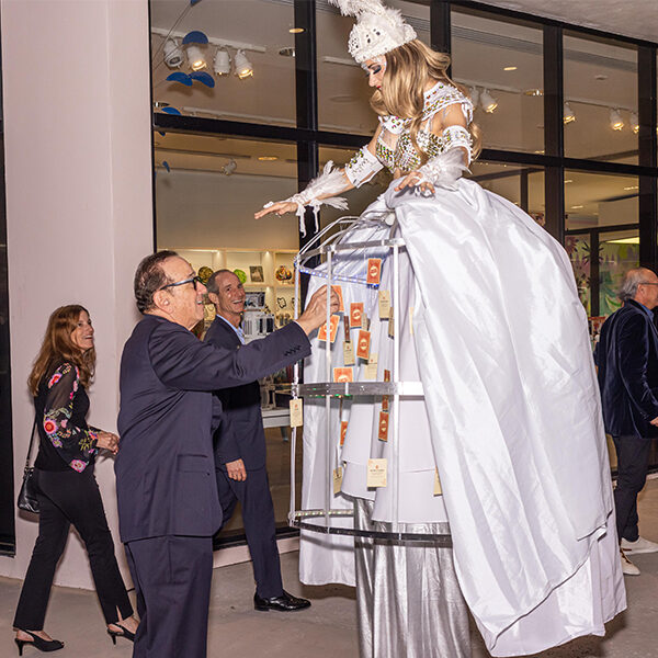 Stilt walker with LED lit cage costume handing out cards to guests during an interactive performance at an upscale event in Miami